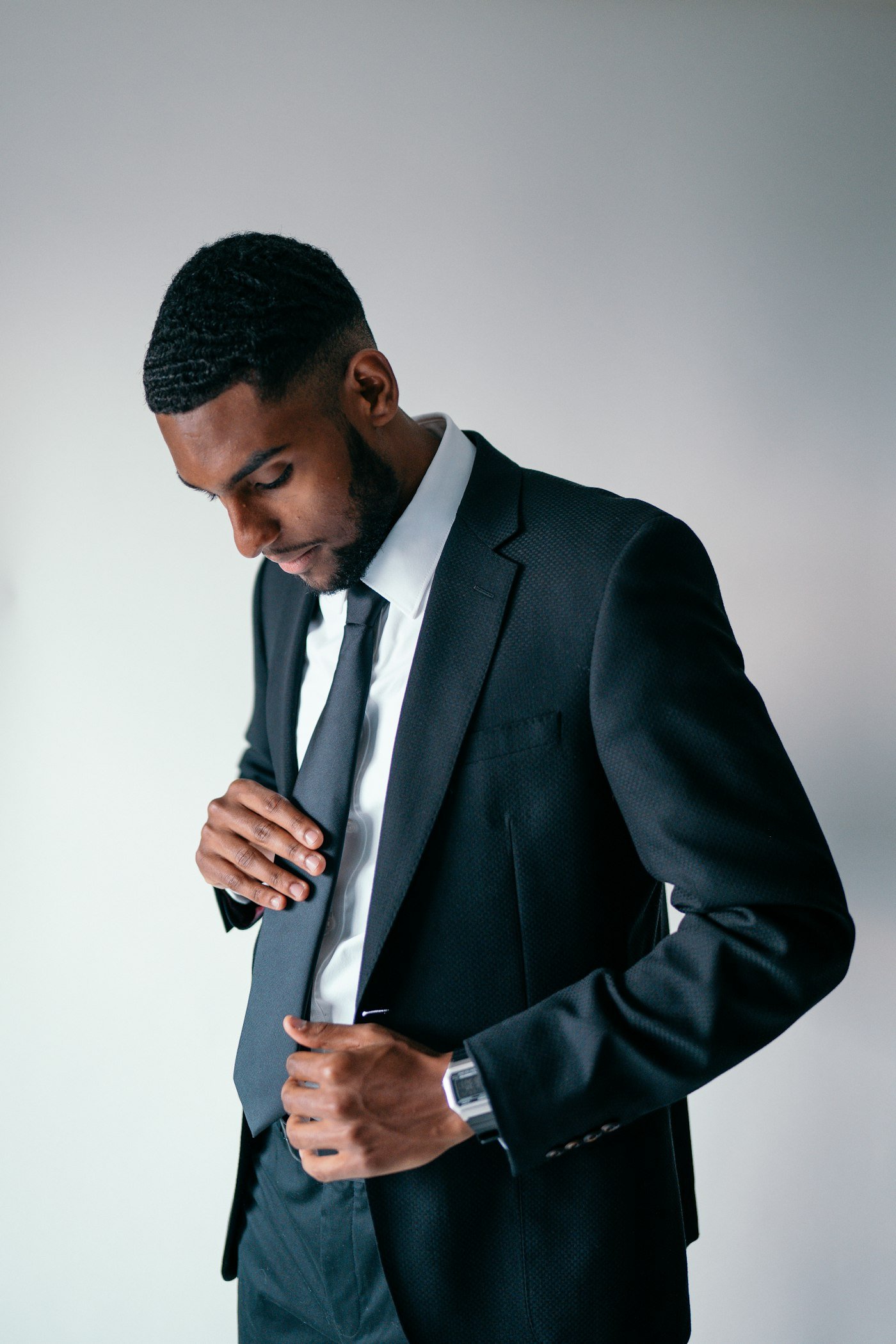 Man in a dark suit adjusting his necktie.