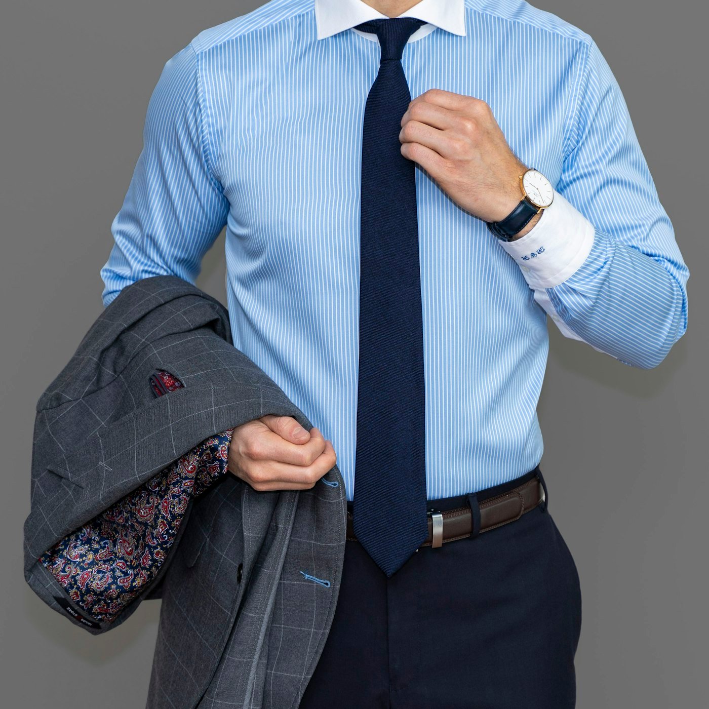 Navy necktie worn with a light blue shirt and grey jacket.